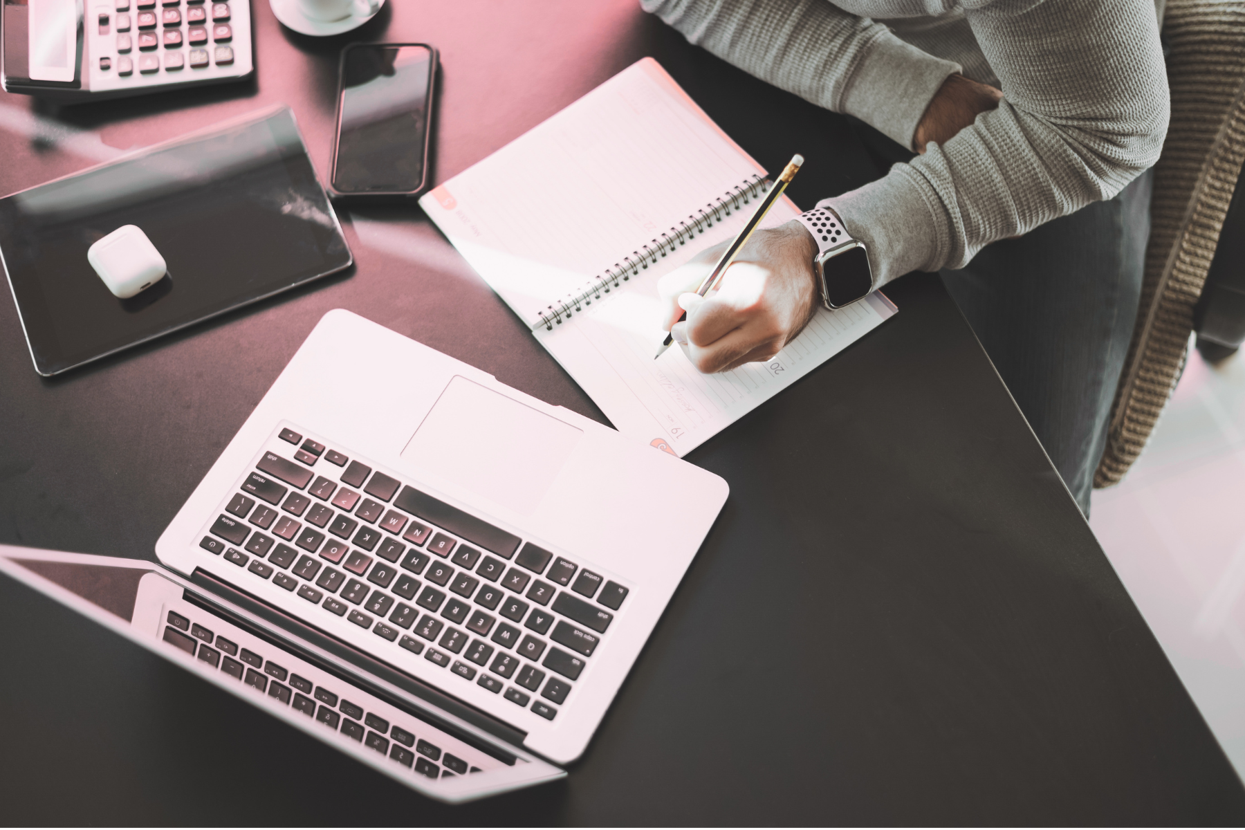 Person writing notes next to a laptop at a desk
